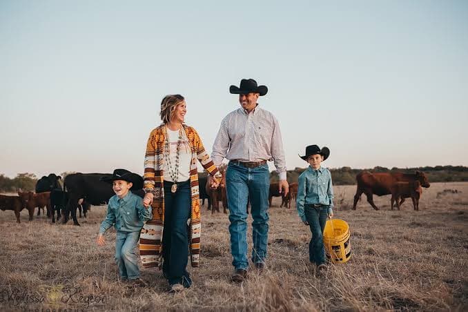 A ranching family walking their pasture at sunset, cattle grazing behind them